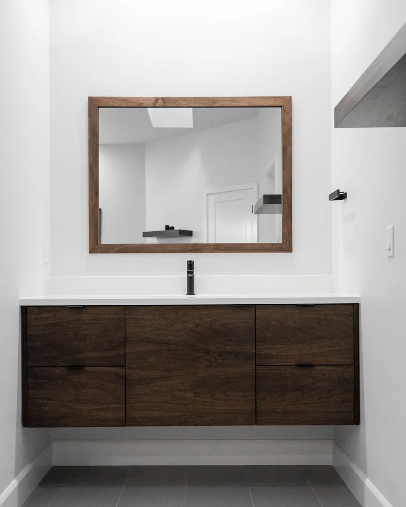 Custom floating walnut vanity with a black faucet and walnut-framed mirror