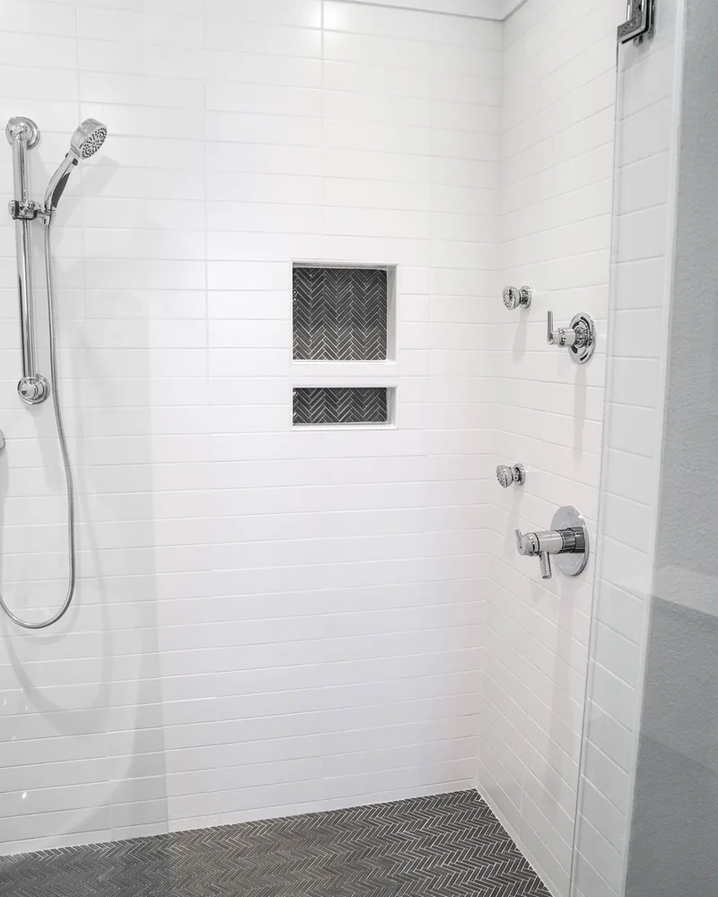 Shower with a herringbone tile floor and stacked niche