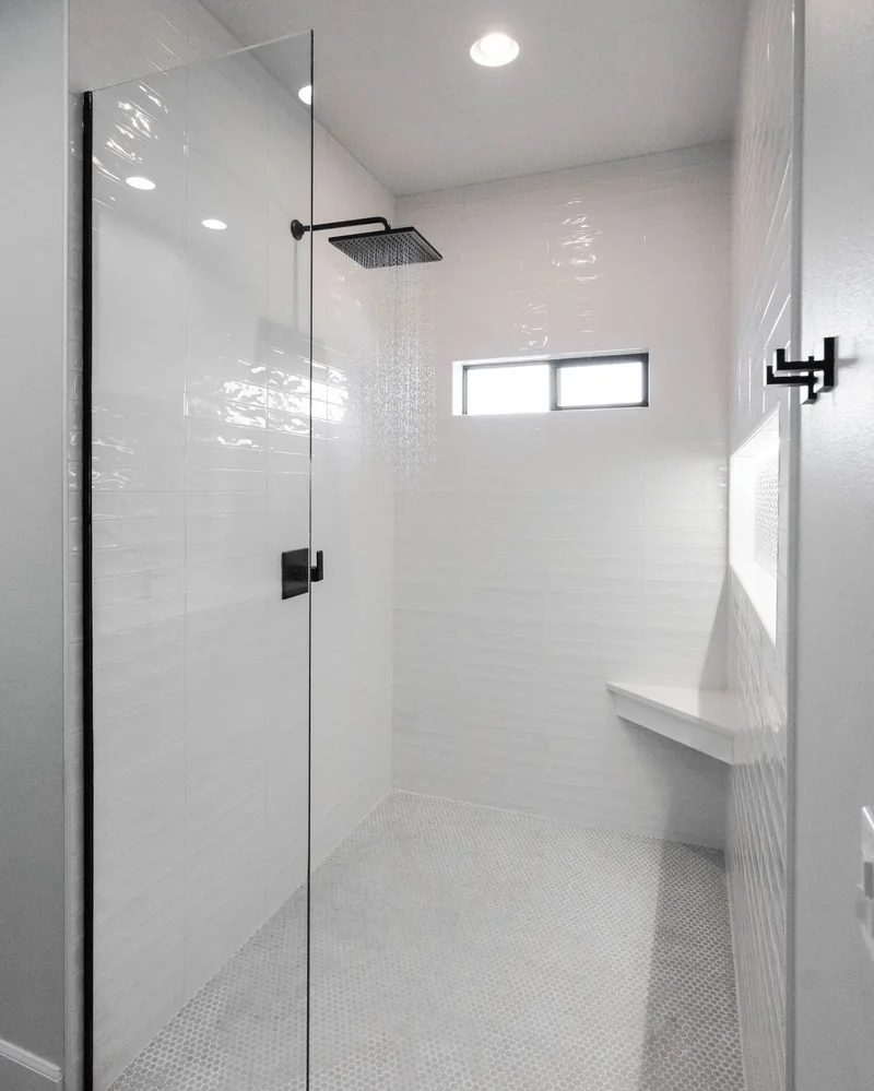 Walk-in shower with a matte black rain head, penny tile floor, and corner bench