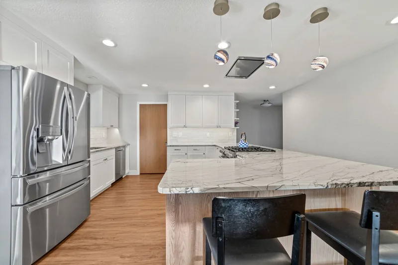 White shaker kitchen with a quartzite peninsula and glass pendants